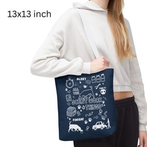 May include: A navy blue tote bag with white illustrations and text, including "ALERT," "ALL THE SCENT WORK THINGS," and "FINISH!" The bag measures 13x13 inches and has a white shoulder strap. The design features a dog, paw prints, and other related icons.