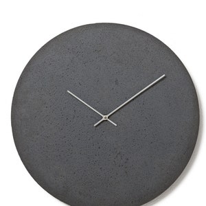 Op de afbeelding: Een ronde, grijze betonnen klok met zilveren wijzers.