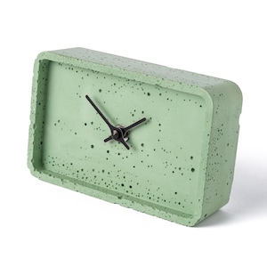 May include: A green concrete clock with black hands. The clock has a textured surface and a rectangular shape.
