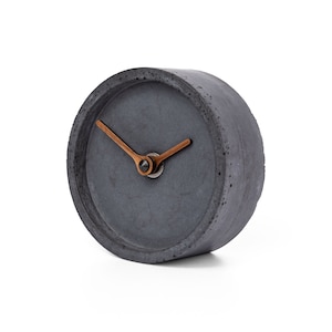 May include: A gray concrete clock with a copper-colored hour hand and minute hand.