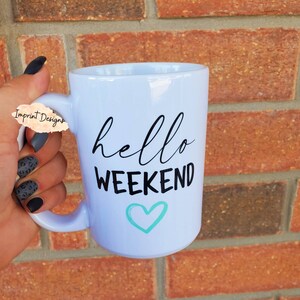 May include: White ceramic mug with black text that reads "hello weekend" and a teal blue heart.