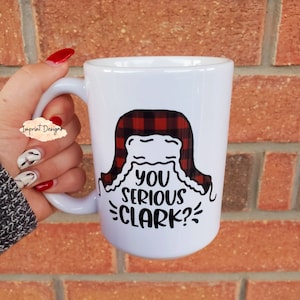 May include: White ceramic mug with a black and red plaid design and the text "You serious Clark?" printed on it.