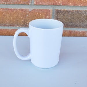 May include: A white ceramic mug with a large handle. The mug is blank and ready to be customized.