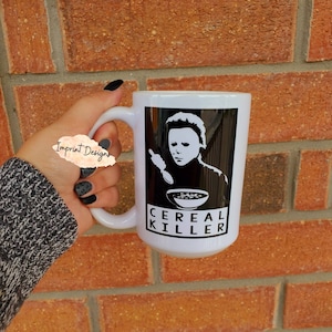 May include: White ceramic mug with a black and white image of a character from a horror movie eating cereal. The text "CEREAL KILLER" is printed on the mug.