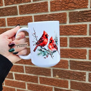 May include: White ceramic mug with a detailed illustration of two red cardinal birds on a branch with green leaves and berries. The mug has a large handle and the text "HAWTHORN & HAZEL" is visible on the side.