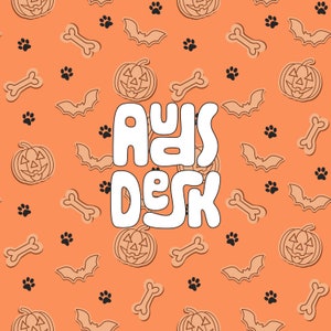 May include: Orange background with a repeating pattern of black paw prints, brown bats, white bones, and orange pumpkins with black jack-o-lantern faces. The text "paws desk" is in white, outlined in black, and centered on the image.