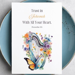 May include: A white card with the text "Trust in Jehovah With All Your Heart. Proverbs 3:5" is displayed on a blue plate. The card features a watercolor illustration of a harp adorned with flowers and a butterfly.