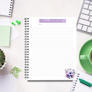 Op de afbeelding: Een spiraalgebonden notitieboek met gelinieerde pagina's, een paars-wit bloemmotief en een schema bovenaan afgedrukt. Een kopje koffie, een toetsenbord en een vetplant zijn ook zichtbaar.