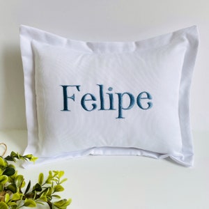 May include: White pillow with a blue embroidered name "Felipe" on it.