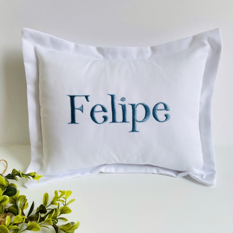 May include: White pillow with a blue embroidered name "Felipe" on it.