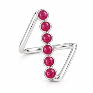 May include: A silver-toned ring featuring a geometric, open-frame design with a vertical row of six round, deep red rubies set in individual bezels. The band forms an angular, zig-zag shape that connects to the top and bottom of the stone setting.