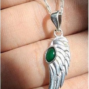 K&ouml;nnte beinhalten: Eine silberfarbene Halskette mit einem Anh&auml;nger in Fl&uuml;gelform und einem gr&uuml;nen Edelstein. Der Fl&uuml;gelanh&auml;nger ist mit federartigen Texturen versehen und h&auml;ngt an einer filigranen Kette. Der gr&uuml;ne Edelstein ist oval und in der Mitte des Fl&uuml;gels gefasst.