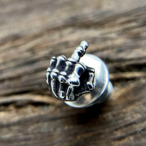 Könnte beinhalten: Silberfarbener Mittelfinger-Ring aus Metall mit strukturierter Oberfläche. Der Ring ist so gestaltet, dass er wie eine Hand aussieht, die den Mittelfinger zeigt.
