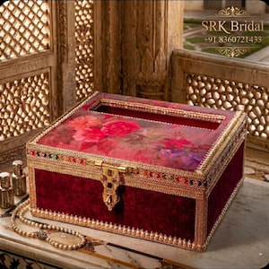 Puede incluir: Una caja rectangular de terciopelo burdeos con una parte superior estampada con flores y ribete dorado. La caja tiene un cierre dorado y está decorada con cuentas de colores. El texto "SRK Bridal" y un número de teléfono son visibles.