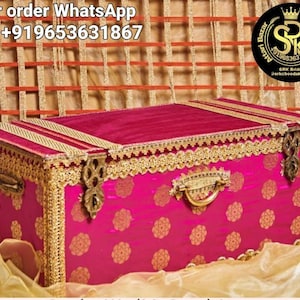 Può includere: Uno scrigno in legno rosa con bordi dorati e una maniglia in ottone. Lo scrigno è decorato con un motivo floreale e ha una fodera in velluto. Lo scrigno è chiuso e si trova su un tessuto dorato.