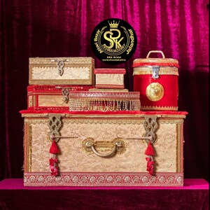 May include: A set of decorative boxes in gold and red with intricate designs and embellishments. The boxes are stacked on top of each other and are perfect for storing jewelry or other small items. The boxes are made of wood and have a traditional Indian design.
