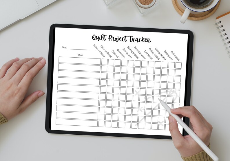 May include: A black and white printable quilt project tracker on a tablet screen. The tracker includes columns for year, pattern, fabric purchased, fabric cut, blocks sewn, quilt top sewn, backing prepared, backing sewn, quilting finished, binding prepared, and quilt washed.