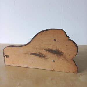 K&ouml;nnte beinhalten: Ein Holzregalhalter mit einem geschwungenen, dekorativen Design. Der Halter ist aus hellem braunem Holz gefertigt und hat eine dunkelbraune Beize. Er hat ein kleines Metallscharnier auf der linken Seite.