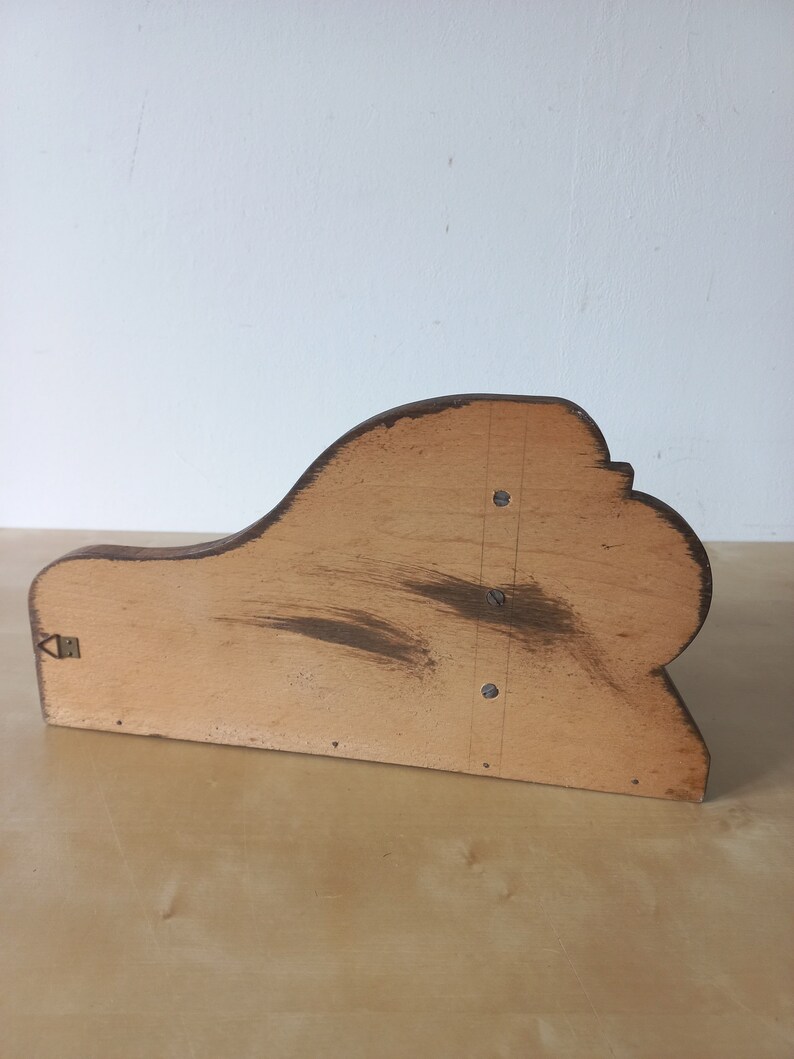 K&ouml;nnte beinhalten: Ein Holzregalhalter mit einem geschwungenen, dekorativen Design. Der Halter ist aus hellem braunem Holz gefertigt und hat eine dunkelbraune Beize. Er hat ein kleines Metallscharnier auf der linken Seite.