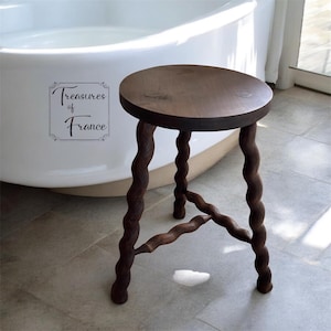 May include: A dark brown wooden stool with a round seat and three intricately carved, twisted legs. The stool is positioned in front of a white bathtub. The text "Treasures of France" is visible.