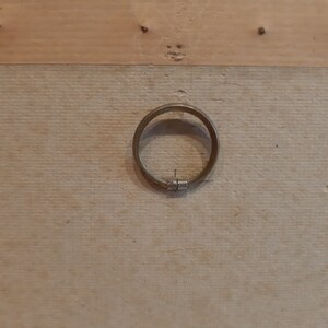 Puede incluir: Primer plano de un marco de madera con un anillo de metal sujeto a la parte posterior. El anillo es circular y tiene una bisagra en un lado.