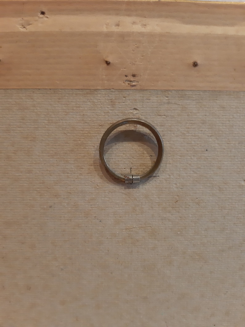 Puede incluir: Primer plano de un marco de madera con un anillo de metal sujeto a la parte posterior. El anillo es circular y tiene una bisagra en un lado.