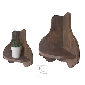 May include: Two wooden corner shelves with a rounded edge and a decorative design. The shelf on the left has a small potted plant on it.