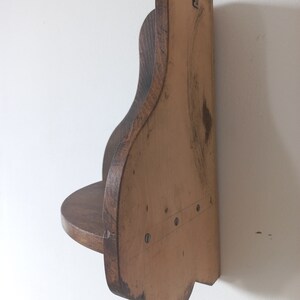 K&ouml;nnte beinhalten: Ein Wandregal aus Holz mit einem geschwungenen, gewellten Design. Das Regal ist in einem dunklen Braunton gebeizt und hat eine kleine, flache Oberfl&auml;che zum Ausstellen von Gegenst&auml;nden.