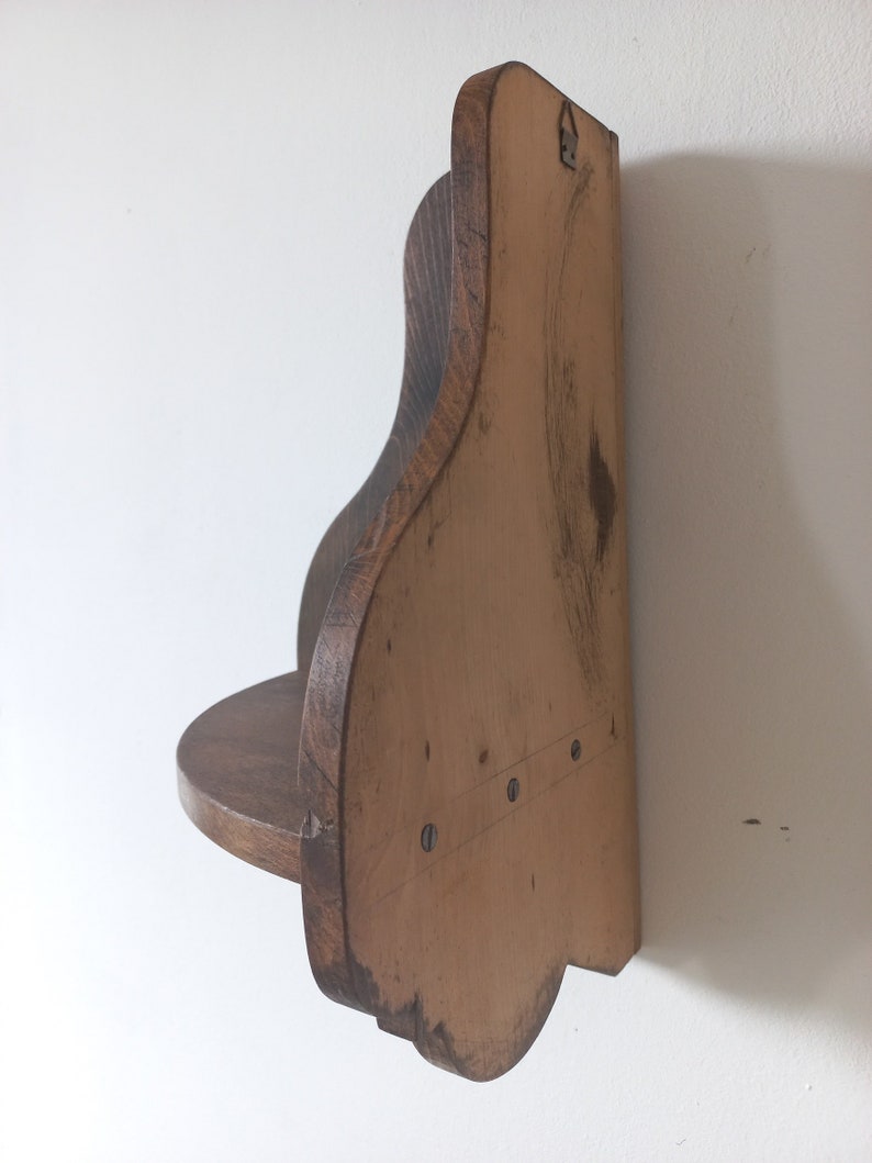 K&ouml;nnte beinhalten: Ein Wandregal aus Holz mit einem geschwungenen, gewellten Design. Das Regal ist in einem dunklen Braunton gebeizt und hat eine kleine, flache Oberfl&auml;che zum Ausstellen von Gegenst&auml;nden.