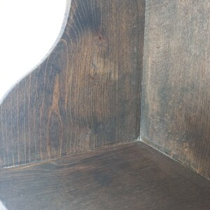K&ouml;nnte beinhalten: Ein dunkelbraunes Eckregal aus Holz mit abgerundeter Kante. Das Regal ist aus unbehandeltem Holz und hat eine nat&uuml;rliche Maserung.
