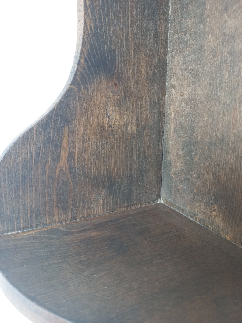 K&ouml;nnte beinhalten: Ein dunkelbraunes Eckregal aus Holz mit abgerundeter Kante. Das Regal ist aus unbehandeltem Holz und hat eine nat&uuml;rliche Maserung.