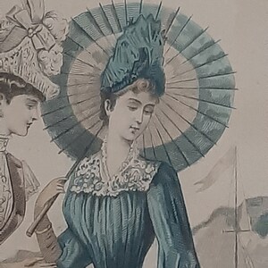 Puede incluir: Una mujer con un vestido azul verdoso con un cuello de encaje blanco y un gran sombrero azul oscuro con una pluma. Lleva un paraguas con una cubierta a rayas blancas y verdes.