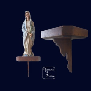 Peut inclure: Une statue blanche de la Vierge Marie avec une robe bleue et une fleur blanche dans la main, debout sur une étagère en bois. L'étagère est fixée à un support en bois avec des sculptures ornées.