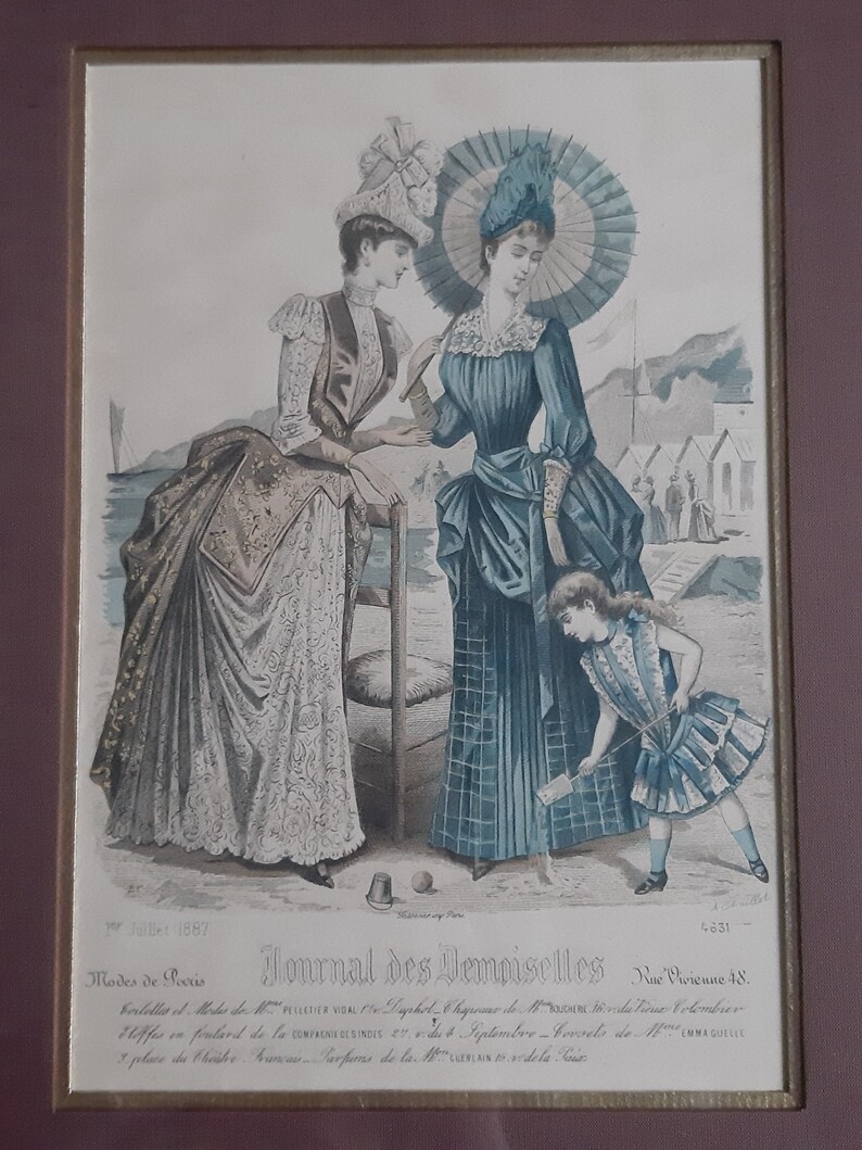 Puede incluir: Una ilustraci&oacute;n vintage de la revista Journal des Demoiselles, julio de 1887, que presenta a tres mujeres con ropa de moda. Dos mujeres est&aacute;n de pie en una playa, una sosteniendo un paraguas, mientras que una ni&ntilde;a peque&ntilde;a con un vestido a rayas juega en la arena. La ilustraci&oacute;n est&aacute; realizada en un estilo delicado, pintado a mano, con colores suaves.