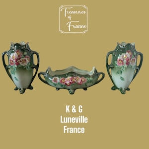 Puede incluir: Un conjunto de tres jarrones antiguos de porcelana verde y blanca con diseños florales. Los jarrones están decorados con rosas rosas y blancas y hojas verdes. El conjunto incluye dos jarrones altos y un cuenco ancho y poco profundo. Los jarrones están marcados con "K&G Luneville France".