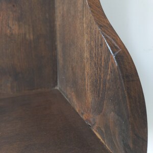 K&ouml;nnte beinhalten: Ein dunkelbraunes Eckregal aus Holz mit abgerundeter Kante. Das Regal ist aus Naturholz gefertigt und hat einen rustikalen Look.