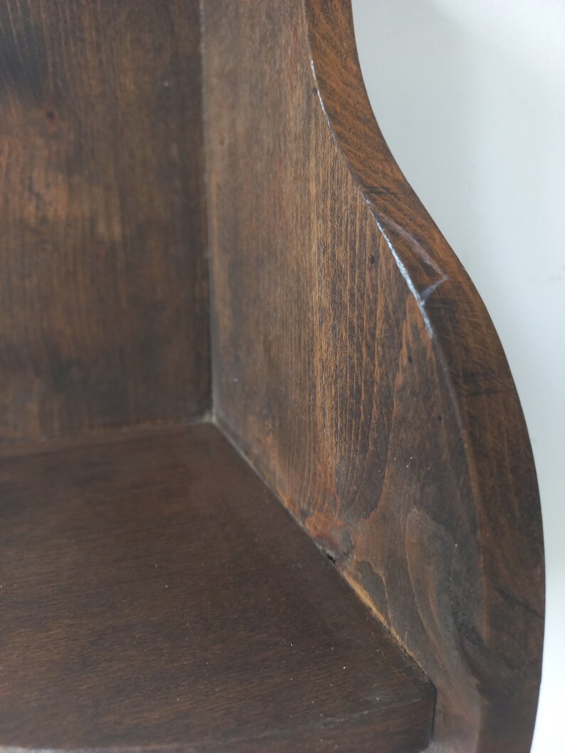 K&ouml;nnte beinhalten: Ein dunkelbraunes Eckregal aus Holz mit abgerundeter Kante. Das Regal ist aus Naturholz gefertigt und hat einen rustikalen Look.