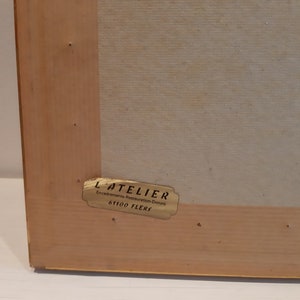 Puede incluir: Una etiqueta dorada con el texto "L'ATELIER Encadrements Restauration Dorure 61100 FLERS" en un marco de madera.