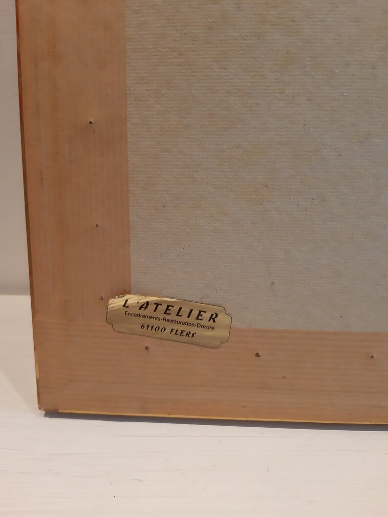 Puede incluir: Una etiqueta dorada con el texto "L'ATELIER Encadrements Restauration Dorure 61100 FLERS" en un marco de madera.