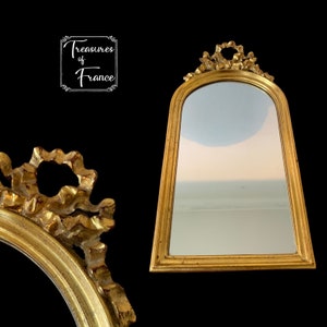 Peut inclure: Un miroir avec un cadre doré, un sommet décoratif et une forme légèrement arrondie. Le miroir est de style vintage et a une finition vieillie.