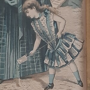 Puede incluir: Una ni&ntilde;a peque&ntilde;a con un vestido azul y blanco con falda con volantes y un lazo en el pelo sostiene una peque&ntilde;a pala. Est&aacute; de pie en un camino de tierra con una mujer con un vestido azul detr&aacute;s de ella.