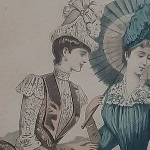 Puede incluir: Dos mujeres con ropa vintage, una lleva un sombrero blanco con un lazo y la otra un sombrero azul con una sombrilla. La mujer con la sombrilla la sostiene sobre su cabeza.