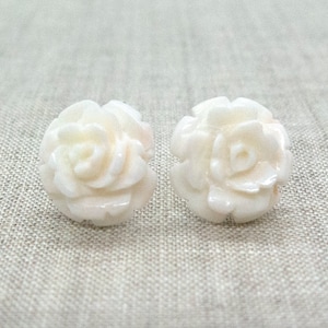 May include: A pair of white shell earrings shaped like roses. The earrings are small and delicate, and they would make a beautiful gift for a special occasion.