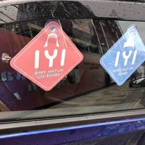 Puede incluir: Dos se&ntilde;ales para la ventana del coche con un dise&ntilde;o de aleta de tibur&oacute;n y el texto "IYI" en blanco. La se&ntilde;al de la izquierda es rosa y dice "Baby Hatun on Board". La se&ntilde;al de la derecha es azul y dice "Baby Alp on Board".