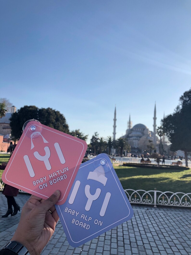 Puede incluir: Dos se&ntilde;ales de coche con un mensaje de beb&eacute; a bordo. La se&ntilde;al de la izquierda es rosa con el texto "Baby Hatun On Board" y la se&ntilde;al de la derecha es azul con el texto "Baby Alp On Board".
