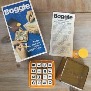 May include: A vintage Boggle word game set. The box, tray, and dice are orange and yellow. The game includes a timer and instructions. The box reads "Boggle" and "Parker Brothers Hidden Word Game."