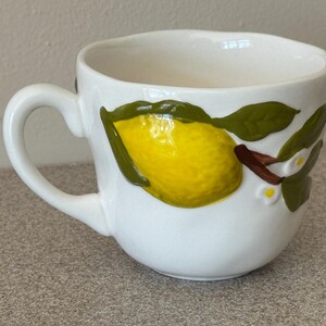 May include: A white ceramic mug with a black handle and the text "But First, Coffee" in a black, handwritten-style font. The mug is on a white surface.