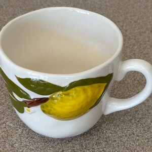 May include: A white ceramic mug with a black handle and the text "But First, Coffee" in a black, bold font. The mug is sitting on a white surface. The mug is approximately 4 inches tall.