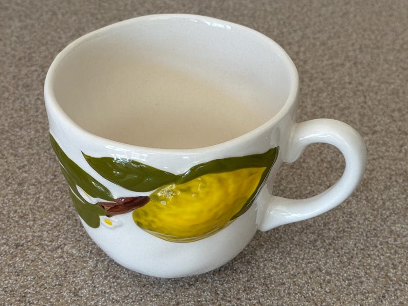 May include: A white ceramic mug with a black handle and the text "But First, Coffee" in a black, bold font. The mug is sitting on a white surface. The mug is approximately 4 inches tall.