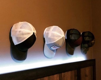 Op de afbeelding: Vier baseballpetten hangen aan een muur. Twee van de petten zijn wit met zwarte kleppen en gaaspanelen. De andere twee petten zijn zwart met witte gaaspanelen.